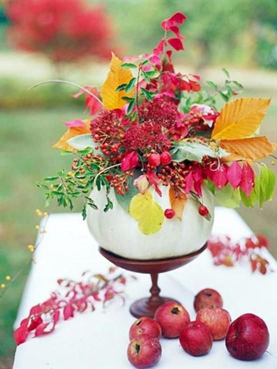 a Thanksgiving centerpiece made of a wooden stand, a white pumpkin, orange leaves and hot red berries plus leaves