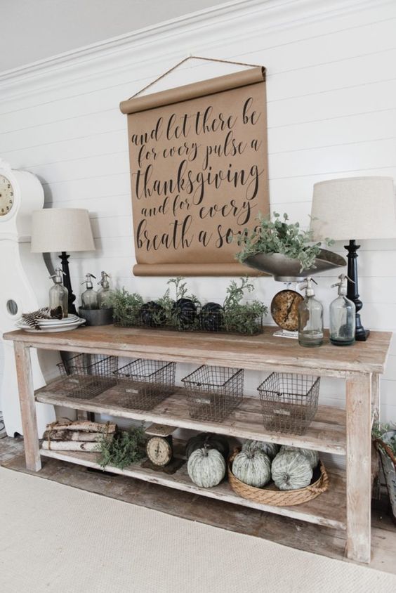a vintage farmhouse console with heriloom pumpkins, metal wire baskets, foliage and a kraft paper sign over it