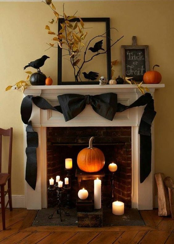 a natural fireplace and mantel with a black ribbon bow, fake birds, fall leaves on branches and lots of candles