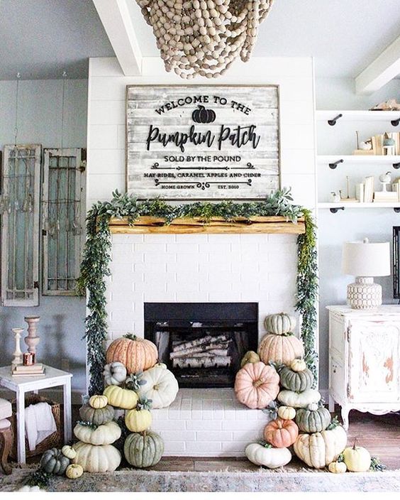 a mantel styled with a fresh greenery garland and heirloom pumpkins stacked next to the fireplace