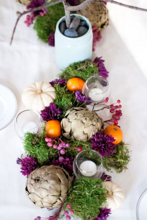 a Thanksgiving centerpiece with artichokes, white pumpkins, moss and purple berries and blooms