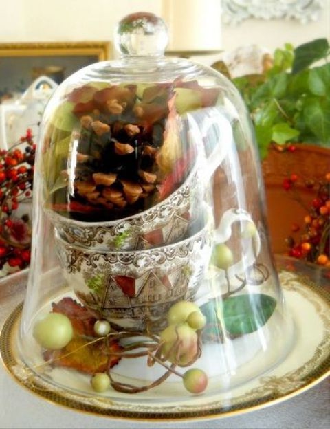 a vintage cloche with a pinecone, vintage cups and fake leaves and apples for a vintage table setting