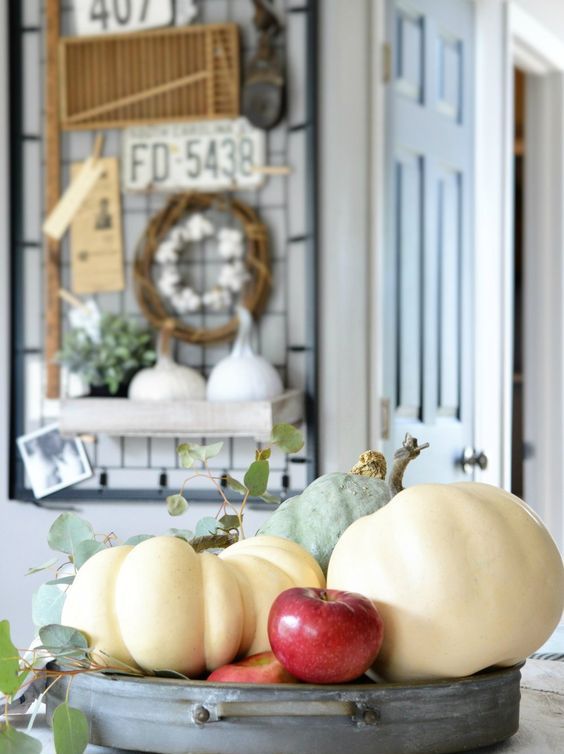 An all natural fall or Thanksgiving centerpiece of a metal bowl, pumpkins, apples and greenery