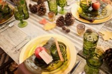 25 an outdoor Thanksgiving tablescape dotted with green glasses and glass plates and foliage and blooms in a birch bark vase