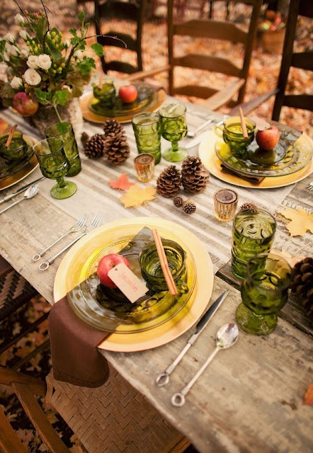 an outdoor Thanksgiving tablescape dotted with green glasses and glass plates and foliage and blooms in a birch bark vase