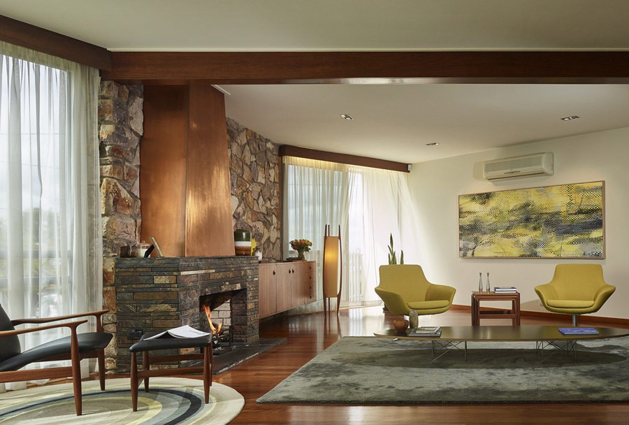 The living room features a large fireplace clad with stone and copper, lemon yellow chairs and a matching artwork plus colorful rugs that cozy up the space