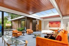 02 The living room features bold orange furniture, catchy glass tables, an entrance to an outdoor space and a large skylight