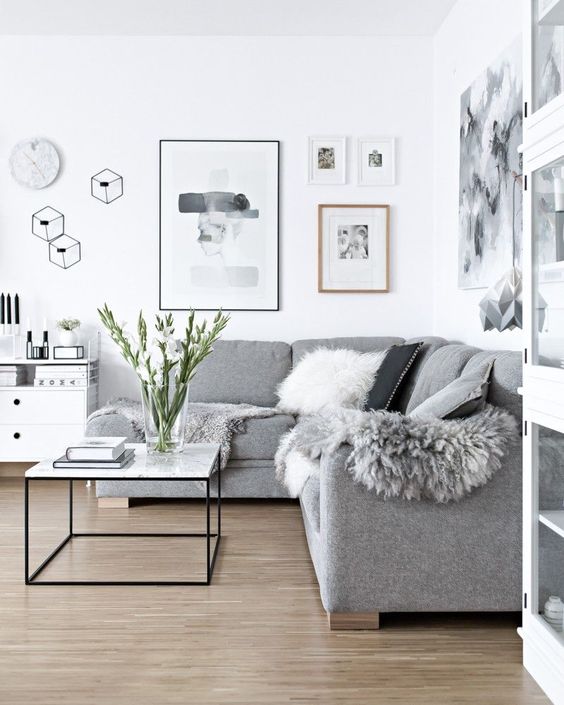 a Scandinavian living room done in white and greys, faux fur and pillows add coziness to the space