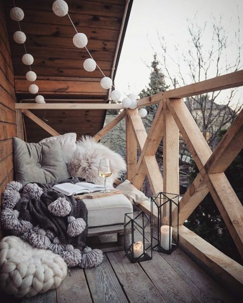 candle lanterns, lights garlands, a seat with fluffy pillows and tassel blanket for a contemporary terrace look