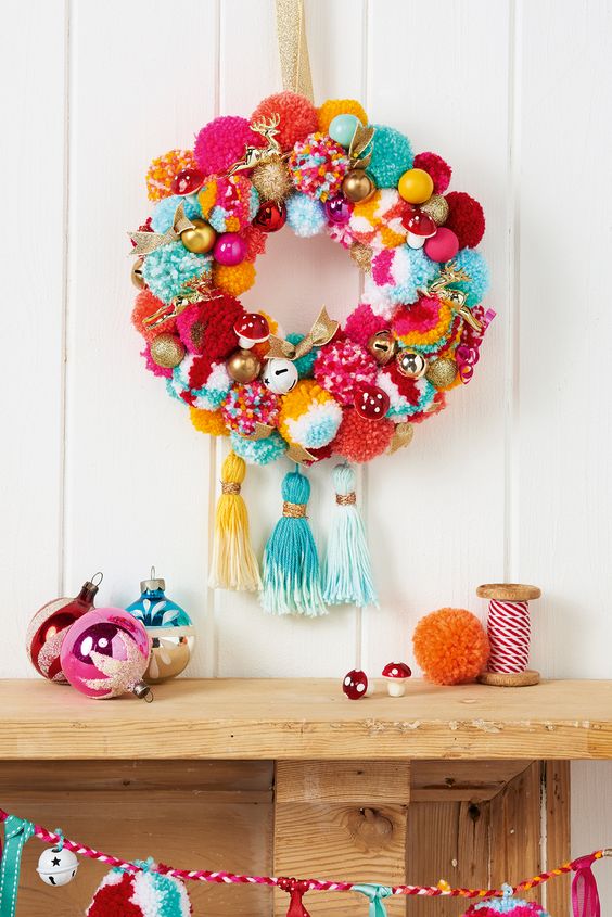 a super colorful and whimsy holiday wreath with pompoms, ornaments, fake mushrooms and large tassels