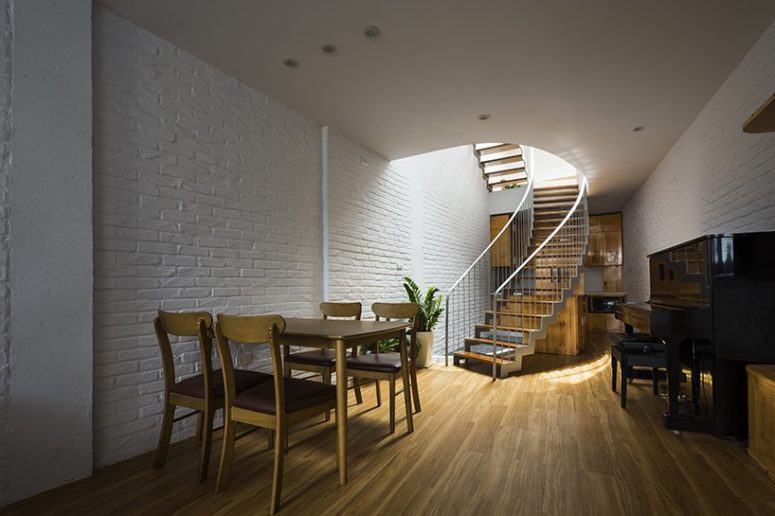 The dining space and kitchen are united in one space, the kitchen is hidden behind the stairs, and there's a piano