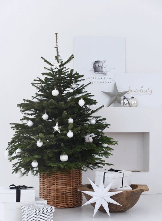 a modern Scandinavian Christmas tree with white ball and star ornaments in a basket looks very laconic and chic