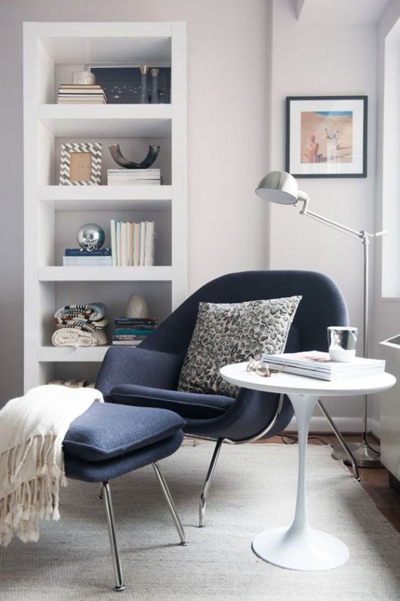 a shelving unit, a comfy chair with a matching footrest, a coffee table and a metal floor lamp that matches the chair frame