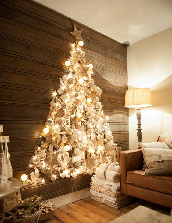 A shiny wall mounted Christmas tree made with lights on the contour and with lots of silver, pearly and white ornaments inside