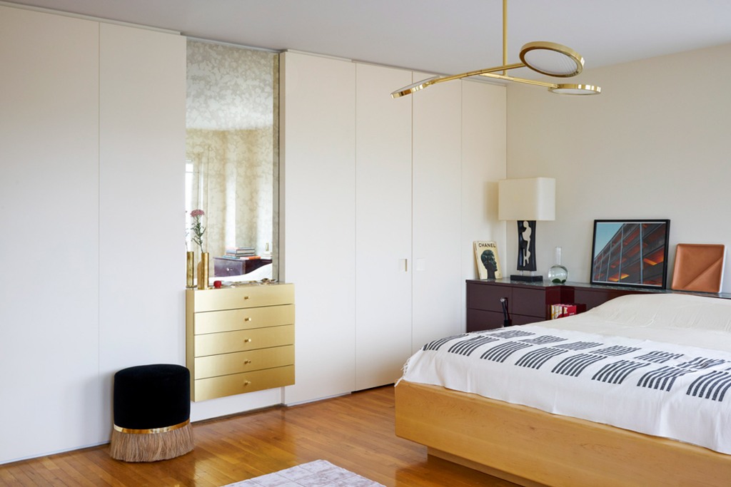 The master bedroom is done in light shades, light-colored wood, a metallic built-in vanity and much closed storage