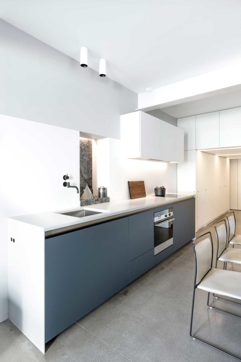 The minimalist kitchen features lower grey cabinets and white countertops, some more white storage units