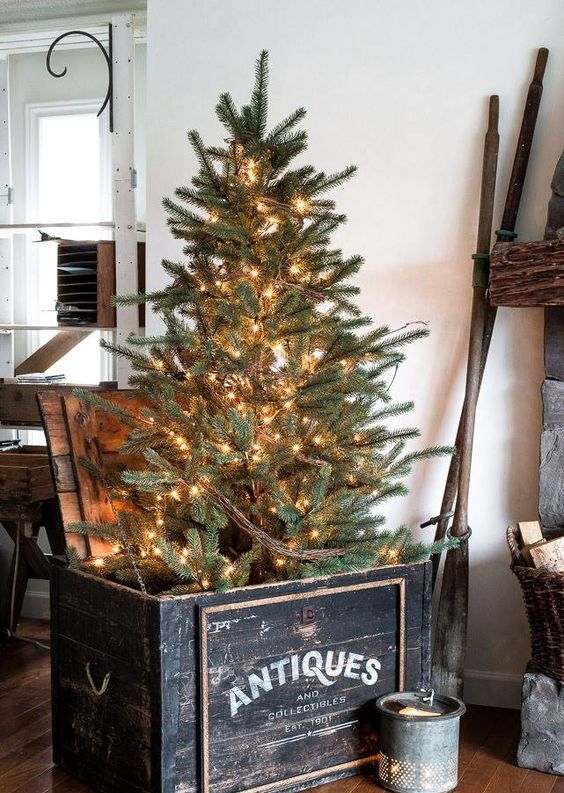 a Christmas tree placed into a vintage black crate and decorated with lights only is a cool rustic and vintage idea