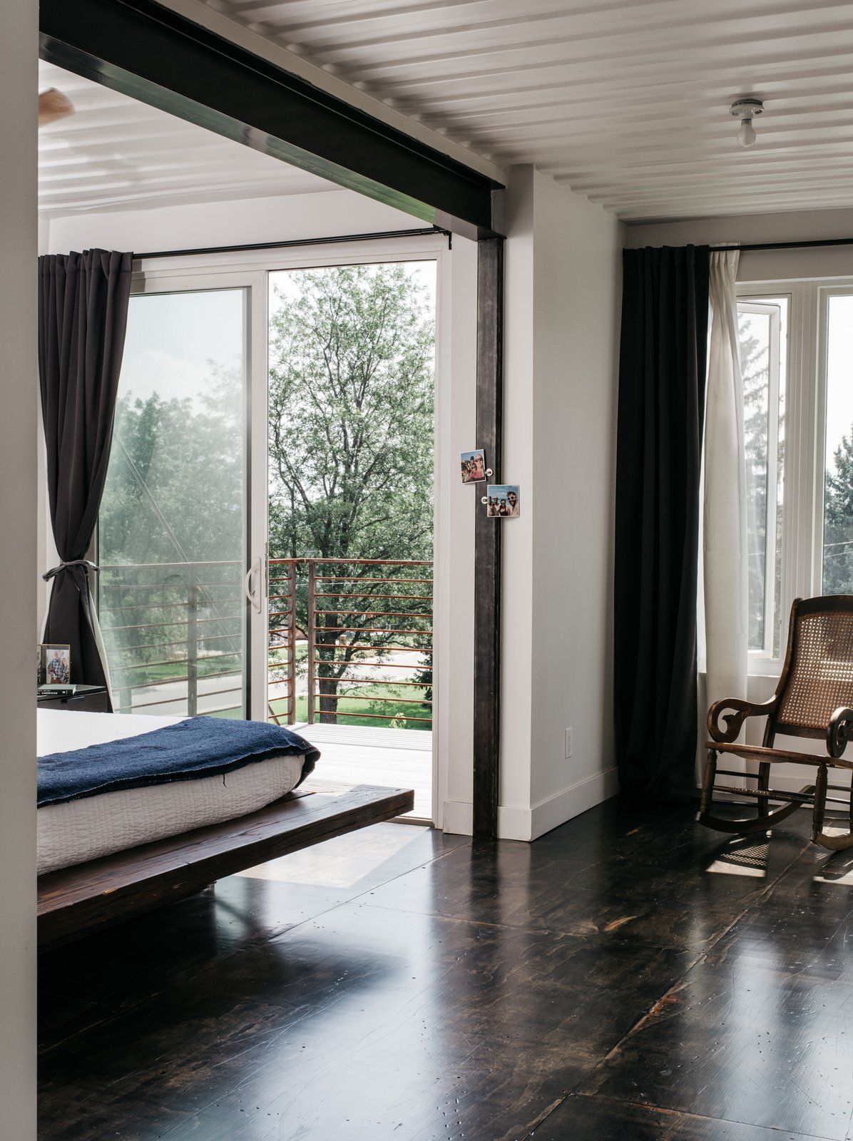 The master bedroom features a platform bed, some chairs, large windows and an entrance to the balcony to enjoy fresh air