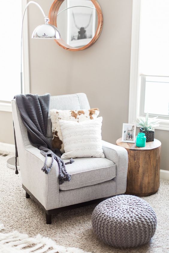 a comfy chair, a knit footrest, a tree stump as a side table, a floor lamp and a round mirror
