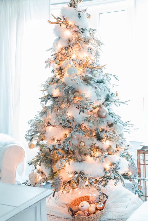 a flocked Christmas tree decorated with cotton to imitate snow, antlers, lights and pinecones and ornaments