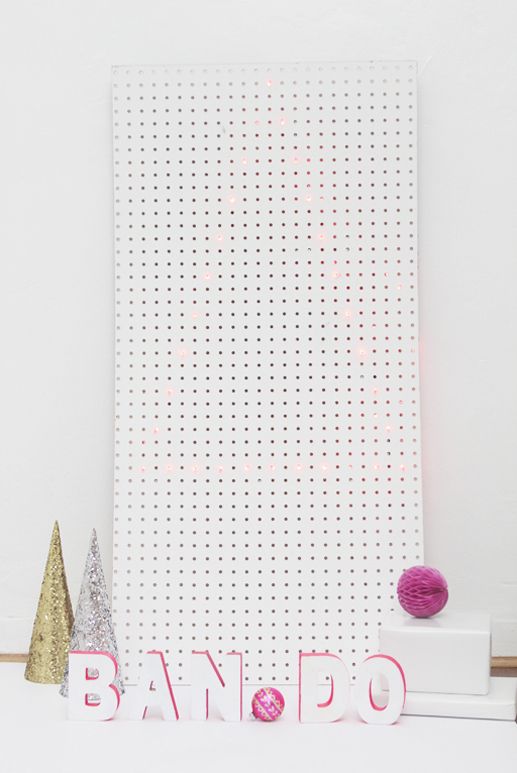 a neon edged Christmas tree on a white pegboard and neon pink letters by the pegboard for a modern whimsy look