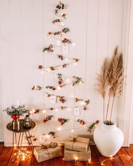 A boho wall mounted Christmas tree of lights, berries and Christmas cards plis pampas grass and blooms around