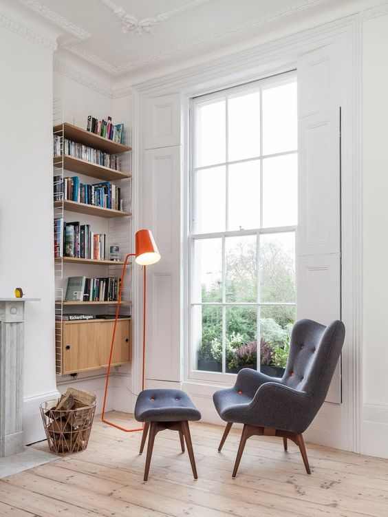 a colorful floor lamp, an upholstered chair with a footrest, a shelving unit on the wall and firewood