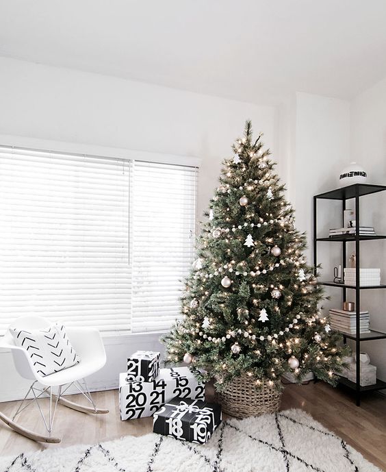 A modern Scandinavian tree with pompom ball garlands, metallic ornaments and tree shaped ornaments plus lights