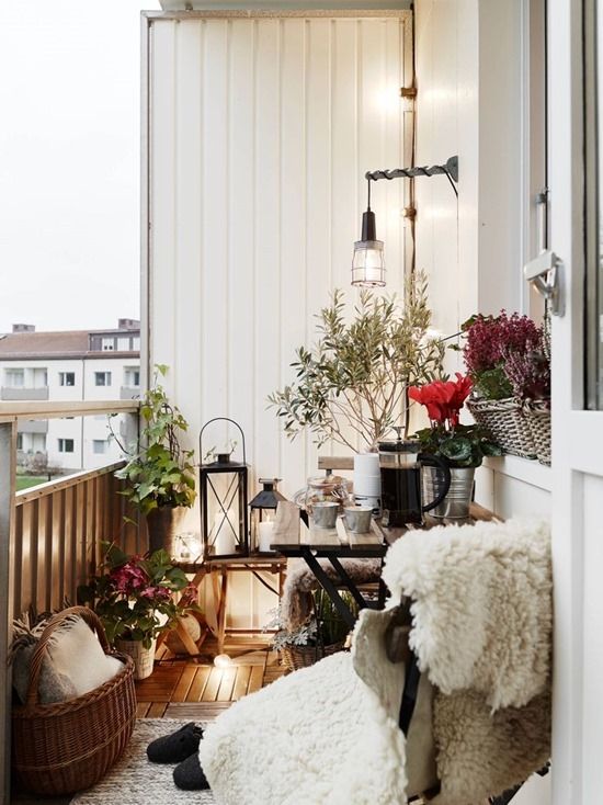 a small space with a chair covered up with faux fur, candle lanterns, baskets and planted flowers