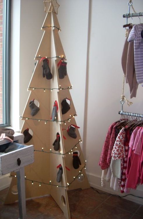 a large plywood Christmas tree decorated with lights and mittens hanging in holes for a simple and modern look