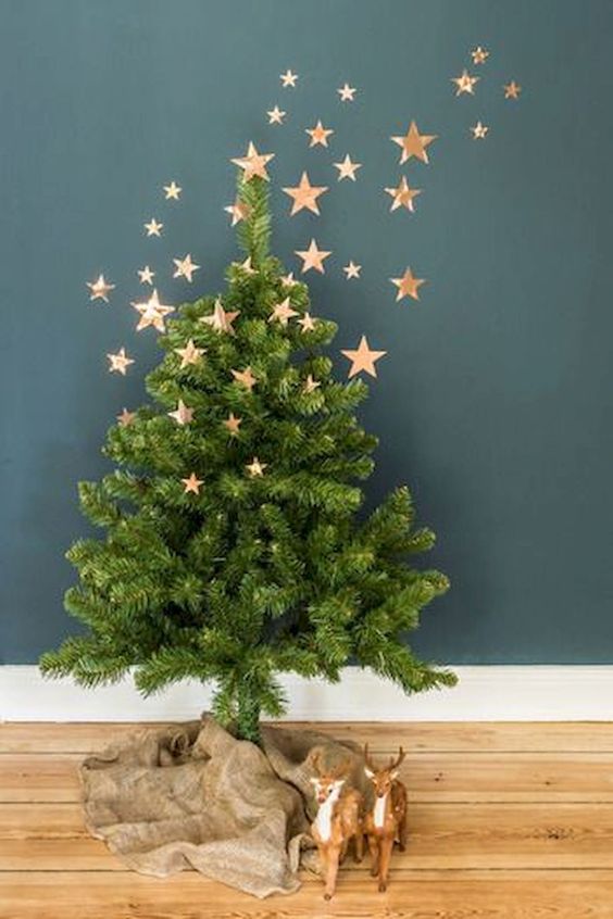 a small Christmas tree with burlap on the floor and copper foli stars as decor going up to the wall