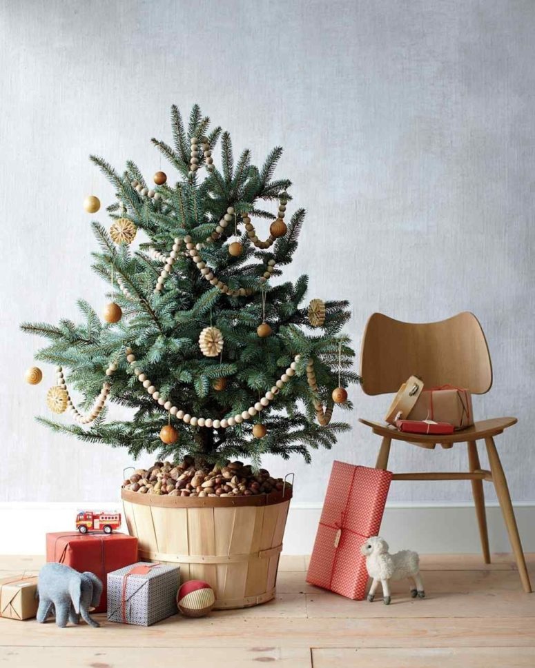 a Christmas tree decorated with wooden ornaments, bead garlands and paper ornaments in a wooden basket with pebbles