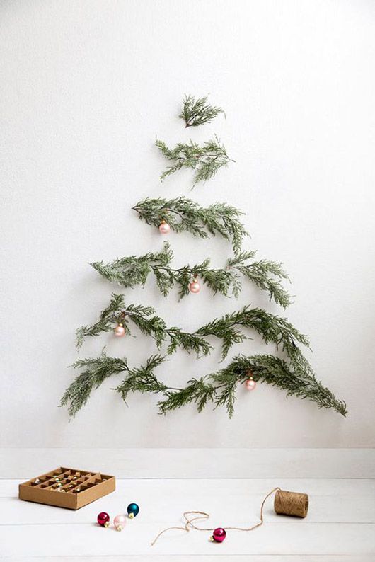 A minimalist wall mounted Christmas tree of evergreens and little copper ornaments on them for an airy feel
