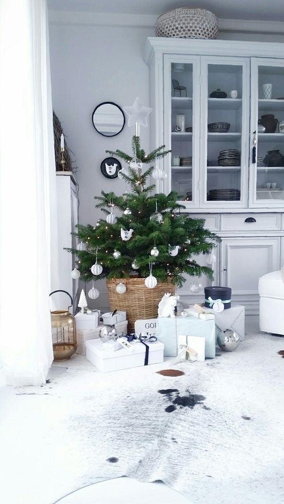 a small Christmas tree with lights and white ornaments plus a basket for a modern feel