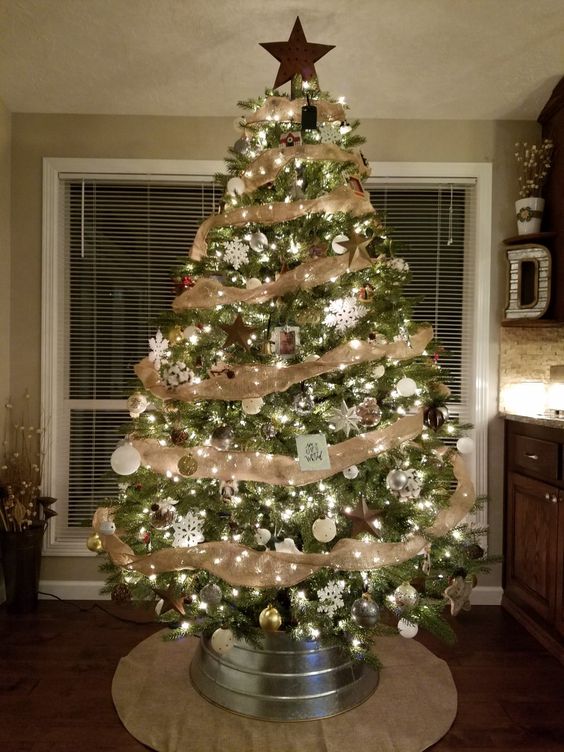 A cozy rustic tree with burlap ribbons, a wooden star on top, metallic ornaments and pinecones and a galvanized tub as a