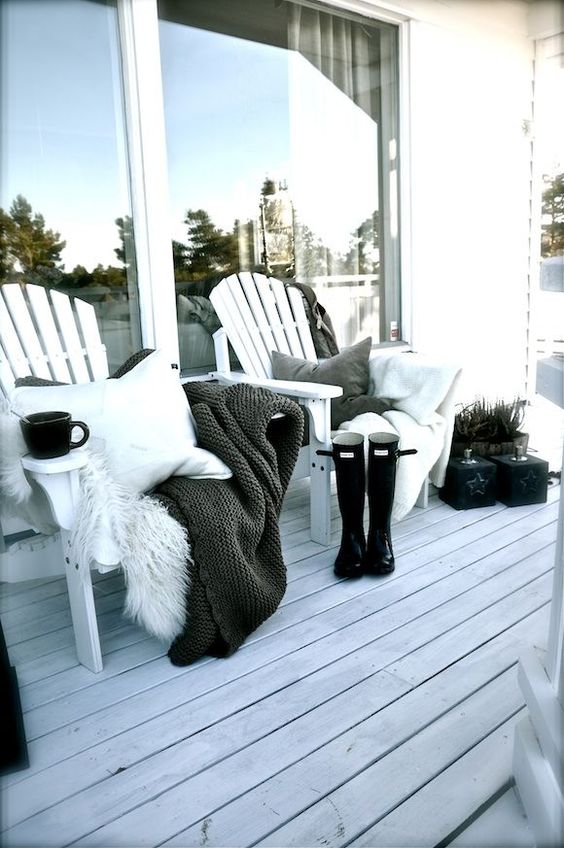 a duo of wooden chairs with pillows, blankets and faux fur, potted plants and a whitewashed deck for a Nordic touch