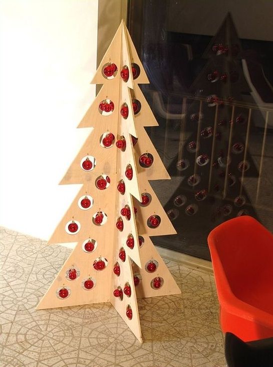 a plywood Christmas tree with holes and little red ornaments hanging in them for a minimalist or Scandinavian space