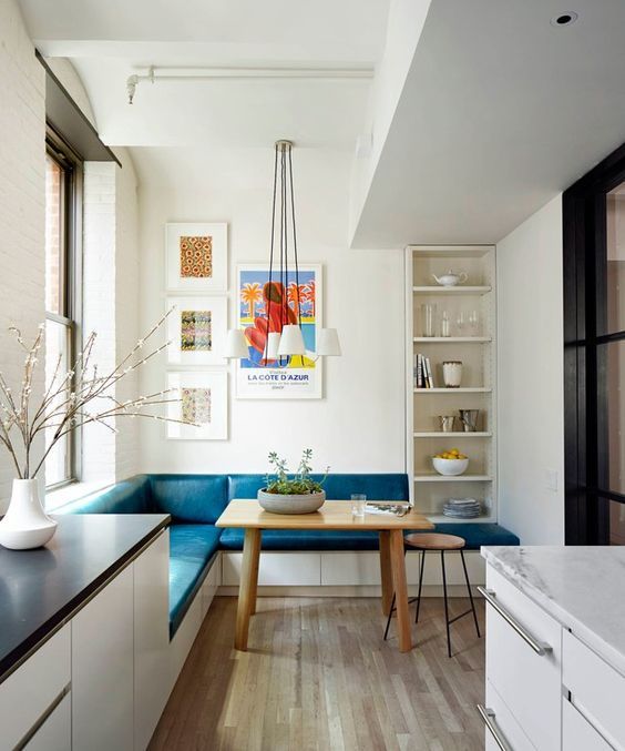 A colorful eat in kitchen nook with an L shaped teal bench and a wooden table doesn't take much space