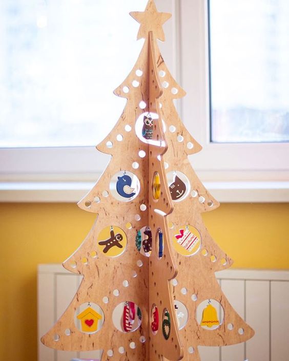 a plywood Christmas tree with holes of various sizes and ornaments hanging in them for a fun and creative look