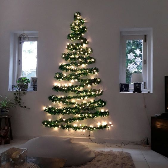 a wall-mounted Christmas tree silhouette done with an evergreen garland and lights for a modern space