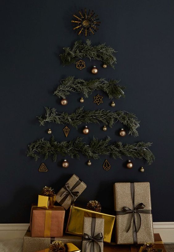 A stylish wall mounted Christmas tree on a black wall of evergreens, lights and brass ornaments