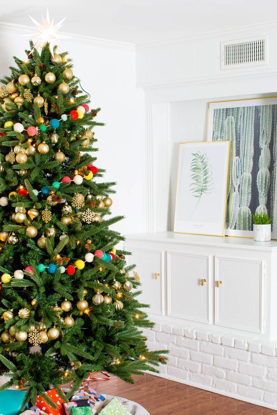 gold ornaments and a colorful pompom garland over the tree is a fun and whimsy idea for Christmas