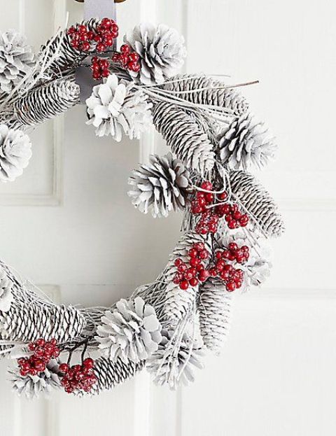 a snowy Christmas wreath of vine, pinecones and fake red berries that add color to it