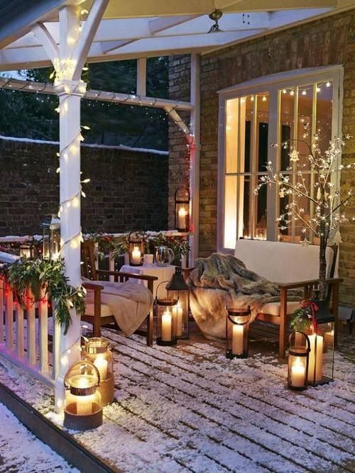 a sofa and a chair with faux fur blankets, candle lanterns, greenery and berry garlands on the railings