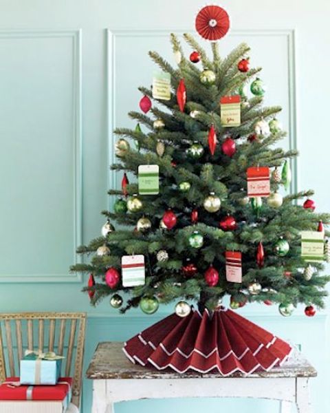 a Christmas tree decorated with silver, green and red ornaments, with Christmas cards and a paper skirt