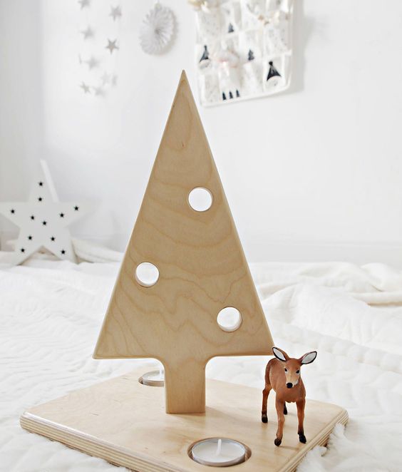 a small plywood Christmas tree on a stand with holes imitating ornaments and some candles