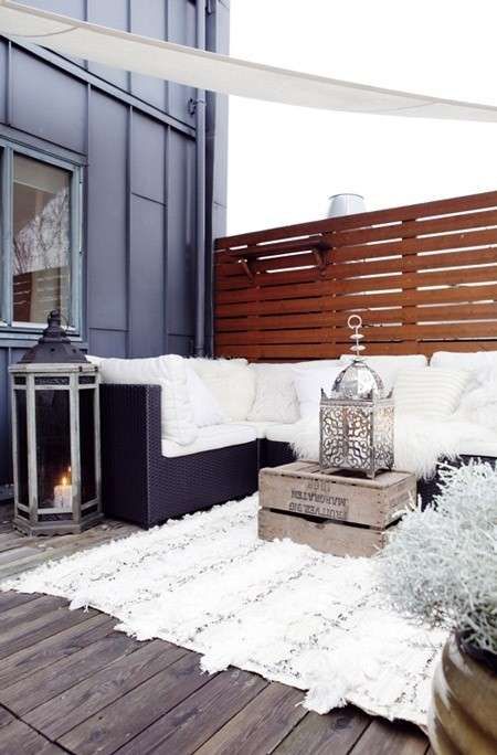 a winter terrace with a fur rug, pillows and fluffy throws, a crate with a decorative lantern and candle lantern