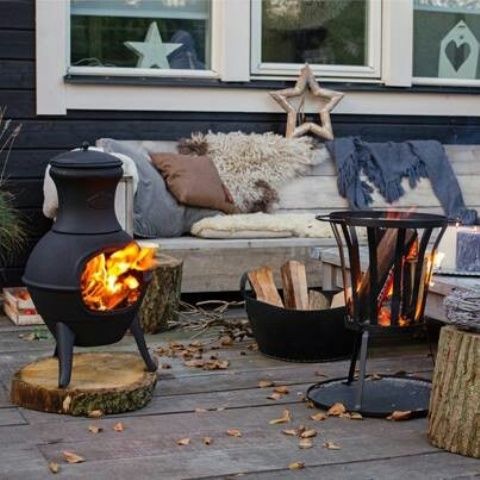 a wooden bench softened with blankets, pillows and faux fur, two fire bowls and firewood in a bucket for a Scandi feel