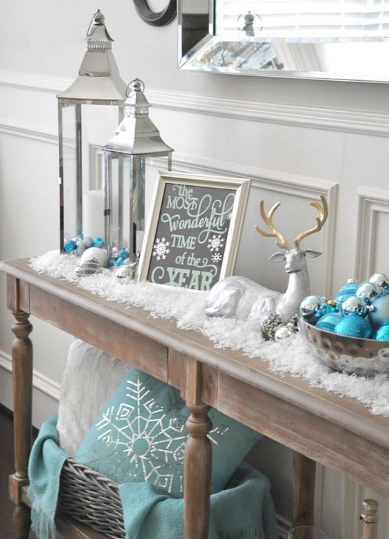 a snowy console with fake snow, ornaments, lanterns, signs and a fake deer for a cozy and cool Christmas look