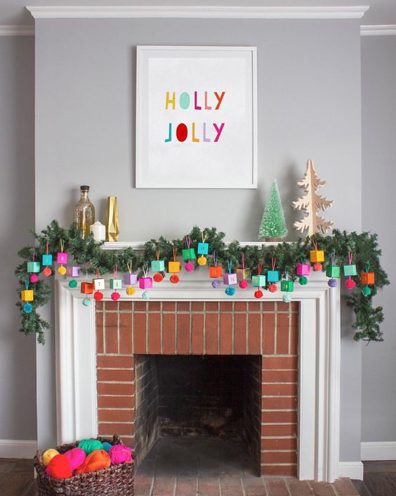 an advent calendar made of colorful boxes and pompoms hanging ona  lush evergreen garland
